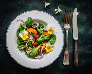 Coloful summer salad with nectarines and edible flowers. Top view.