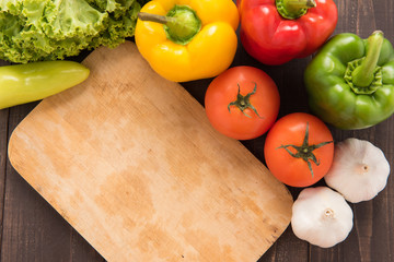 Cutting board with vegetables on wooden background.