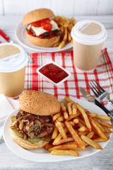 Tasty burger and french fries on plate, on wooden table background. Unhealthy food concept