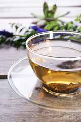 Cup of herbal tea with flowers on wooden table, closeup