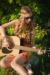 Young woman sitting on a field and playing guitar