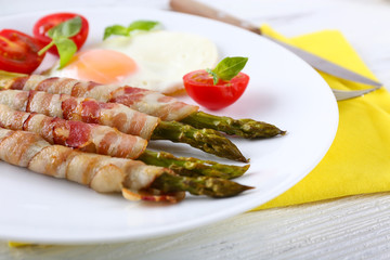 Dish of asparagus with bacon and egg in plate on table, closeup