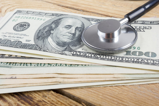 Financial analysis, audit or accounting - Stethoscope over dollar bills on wooden table. Medical costs, financial concept