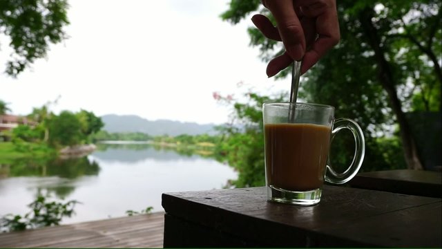 Stirring hot coffee with nature background