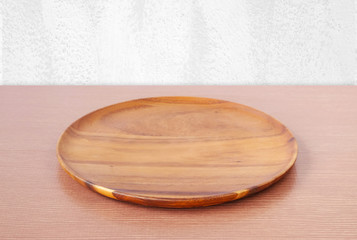 Empty round wooden tray on table over white wall.