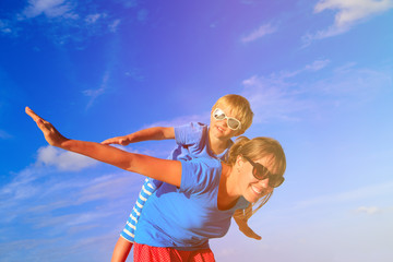 Mother and little son playing airplane on summer sky