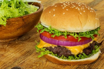 Burger close up with salad on side, horizontal composition on wooden background