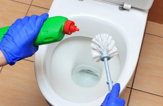 Hand of woman in blue glove cleaning toilet bowl