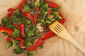 Vegetables mix baked in the oven on paper on the wooden table with aubergine, red bell pepper, brussels sprout, pumpkin seeds, basil and olive oil.