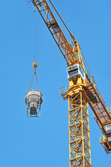 Crane lifting concrete mixer container against blue sky