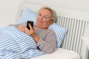Ältere Frau krank mit Handy im Bett