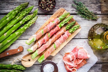 Fresh organic asparagus wrapped in Parma ham on a cutting board