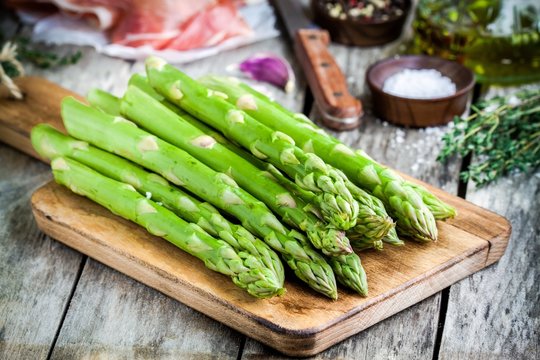Fresh organic asparagus on a cutting board with Parma ham