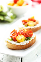 Tasty fresh bruschetta with tomatoes on plate on white wooden ba