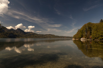 A view on a lake with a small cabin and mountains and clouds in the background