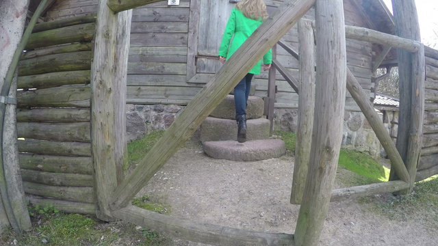 girl in green coat open wooden gate and climb on stone stair. 4K