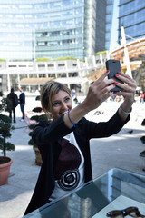 A beautiful young woman smiling and taking herself a selfie in a square in Milan