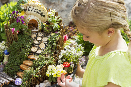 Child Looking At Fairy Garden In A Flower Pot Outdoors