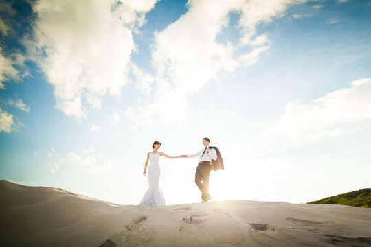 Bride and groom holding hands and running through the sand on th