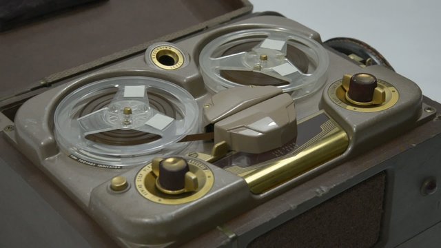 A hand starts and stops playing an old portable tube recorder