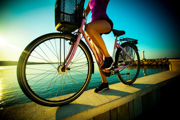 Beautiful streight woman with bicycle on sunset near a sea