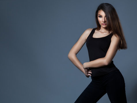 Fashion woman standing over grey background in black clothes.