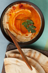 A bowl of hummus with olive, red pepper and pita bread.