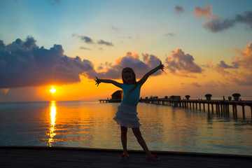 Fototapeta premium Silhouette of adorable little girl on wooden jetty at sunset
