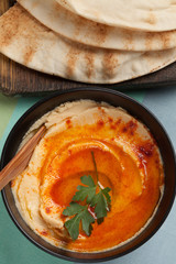 A bowl of hummus with olive, red pepper and pita bread.