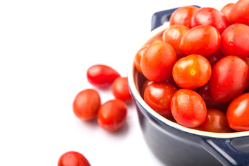 Bite sized red cherry grape tomato in blue pot over white background
