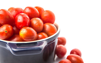 Bite sized red cherry grape tomato in blue pot over white background