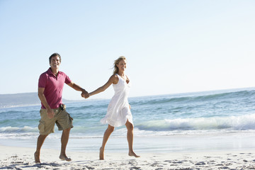 Fototapeta na wymiar Young Couple Walking Along Sandy Beach On Holiday