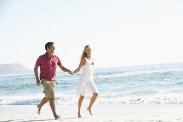 Fototapeta na wymiar Young Couple Running Along Sandy Beach On Holiday