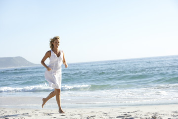 Fototapeta na wymiar Casually Dressed Young Woman Running Along Beach