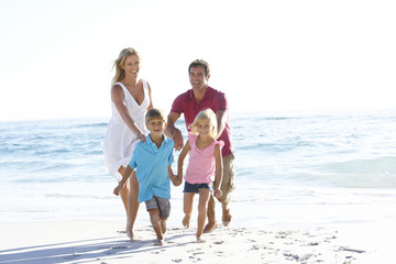 Fototapeta na wymiar Young Family Running Along Sandy Beach On Holiday