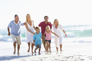 Three Generation Family On Holiday Running Along Beach