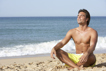 Fototapeta na wymiar Young Man Wearing Swimming Costume Sitting On Beach