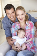 Obraz premium Young Family With Baby Relaxing On Sofa At Home