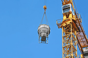 Crane lifting concrete mixer container against blue sky