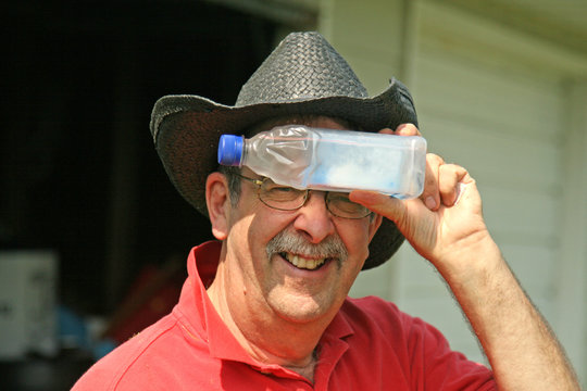 Senior with cowboy hat holds water bottle to forehead in hot sun