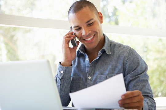 Young Man On Phone Using Laptop At Home