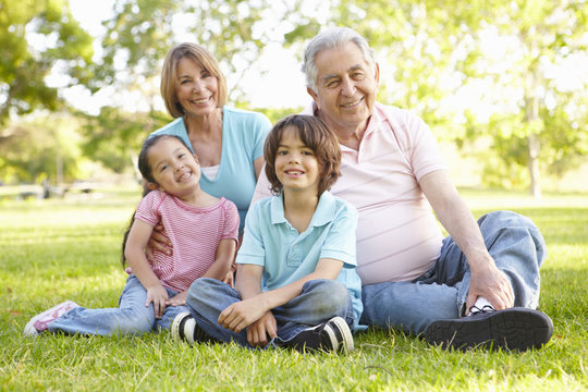 Hispanic Grandmother And Grandfather Relaxing With Grandchildren In Park
