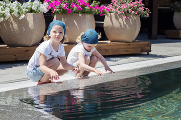 Funny little girls (sisters) are playing near the pool.