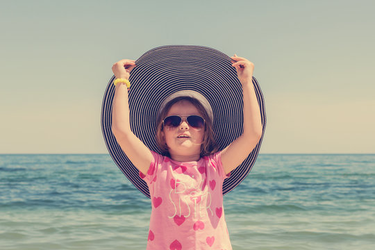 Funny little girl in a big striped hat on the beach. The image i