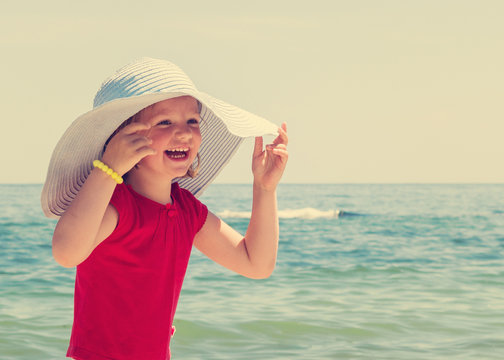 Funny little girl in a big hat on the beach. The image is tinted