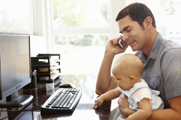 Hispanic father with baby working in home office