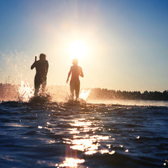 Glückliche junge Menschen laufen und springen am See beim Sonnenuntergang