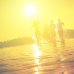 Glückliche junge Menschen laufen und springen am See beim Sonnenuntergang