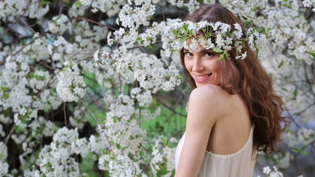 Young beautiful woman in wreath enjoying smell of blooming tree