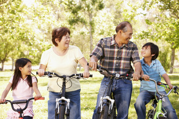 Fototapeta na wymiar Asian grandparents and grandchildren riding bikes in park